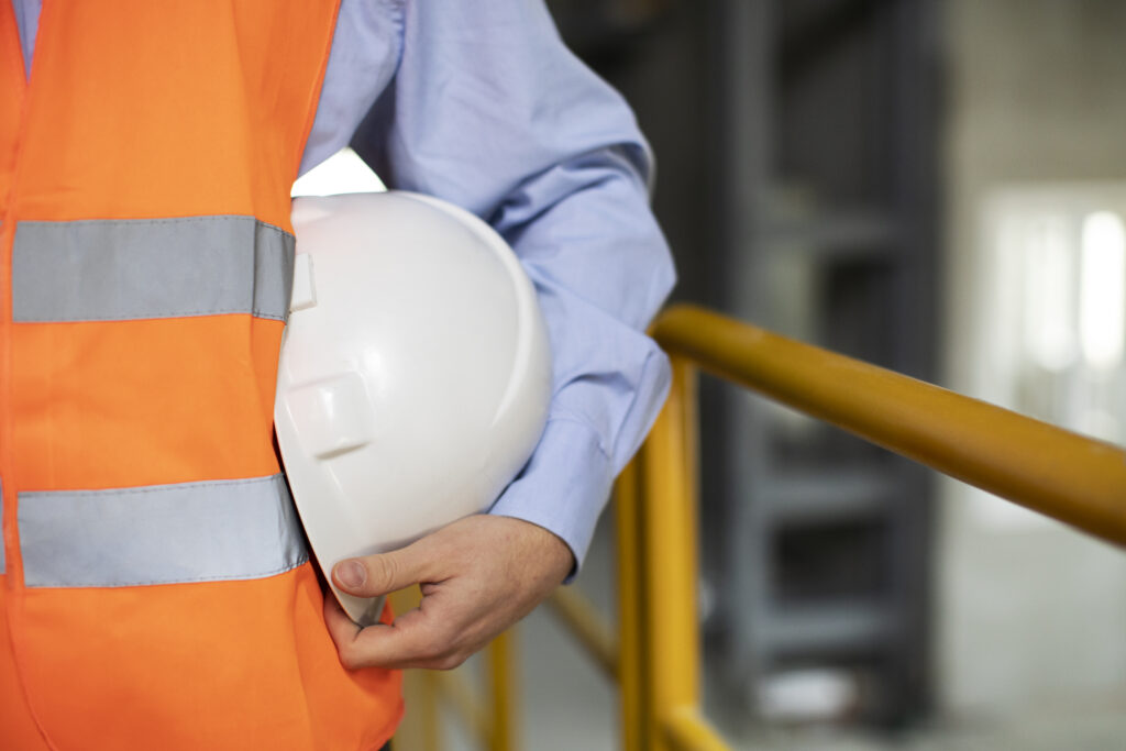 Industrial worker holding safety helmet and wearing high-visibility vest on a construction site