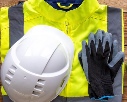 “High-visibility safety jacket with hard hat and protective gloves on wooden surface – workplace PPE for safety”