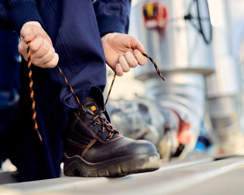 Worker tying laces of protective boots for workplace safety on an industrial construction site.